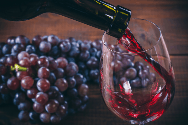 red wine being poured into a glass with grapes behind it